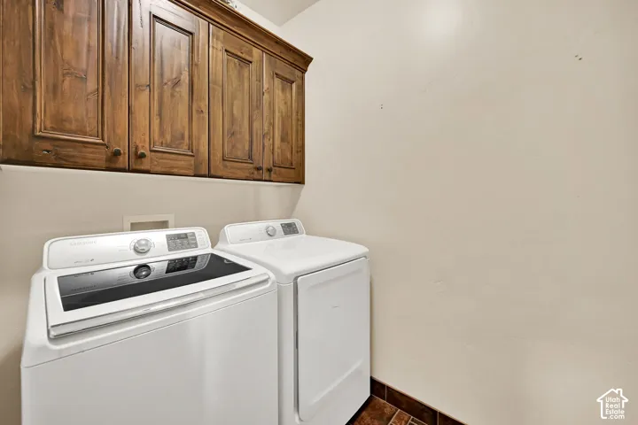 Laundry area featuring rich wood cabinetry with crown molding, light-toned walls, and a tiled floor