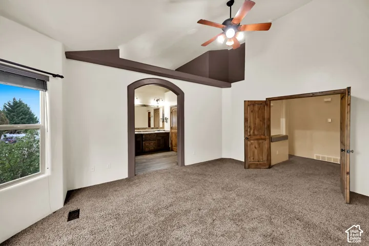 Spacious room featuring vaulted ceilings, a ceiling fan, and carpet flooring