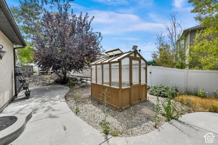Backyard featuring a freestanding greenhouse with wood-finish framing, a gravel bed, concrete pathways, and a privacy fence