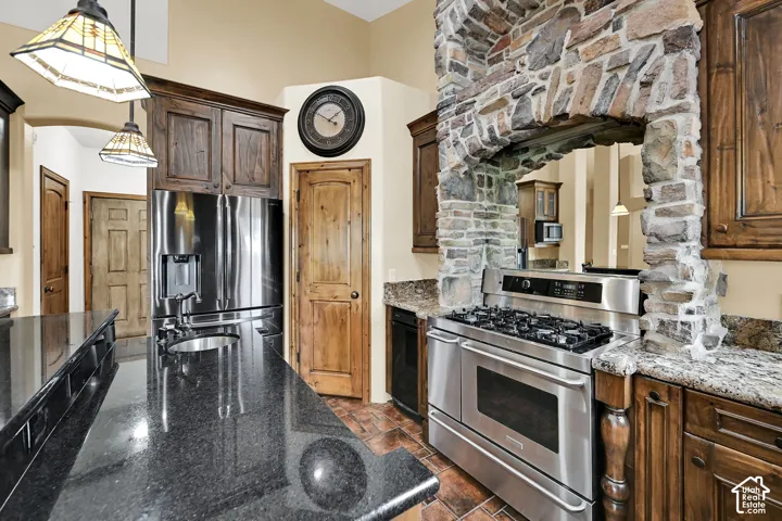 Gourmet kitchen featuring a stone-clad range hood, stainless steel gas range, and a spacious island with a black granite countertop and integrated sink