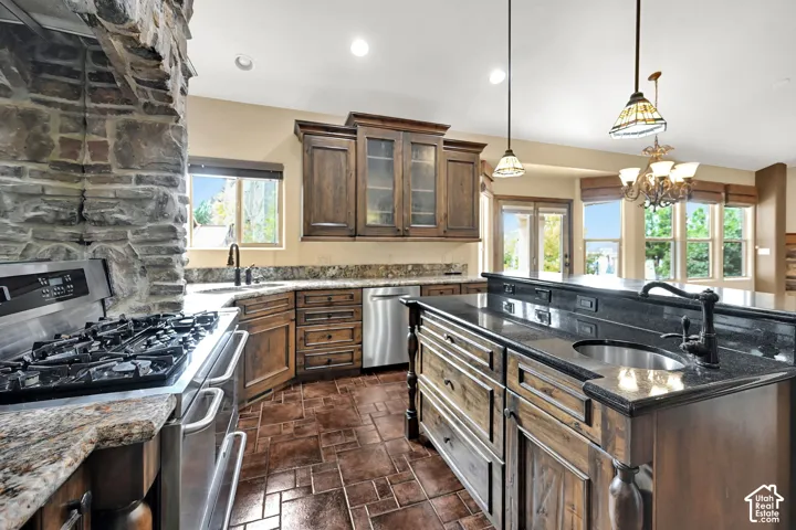 Expansive kitchen featuring a stone accent wall, stainless steel gas range, wood cabinetry, granite countertops, and a large island with a secondary sink