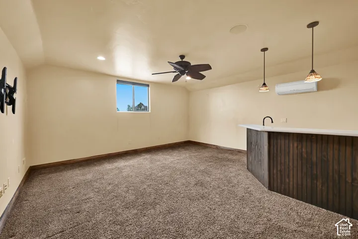Spacious room featuring a built-in bar with a white countertop and dark wood paneling, pendant lighting, and a ceiling fan