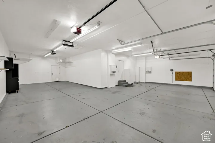 Spacious two-car garage featuring a painted concrete floor, multiple fluorescent light fixtures, and two overhead garage door openers