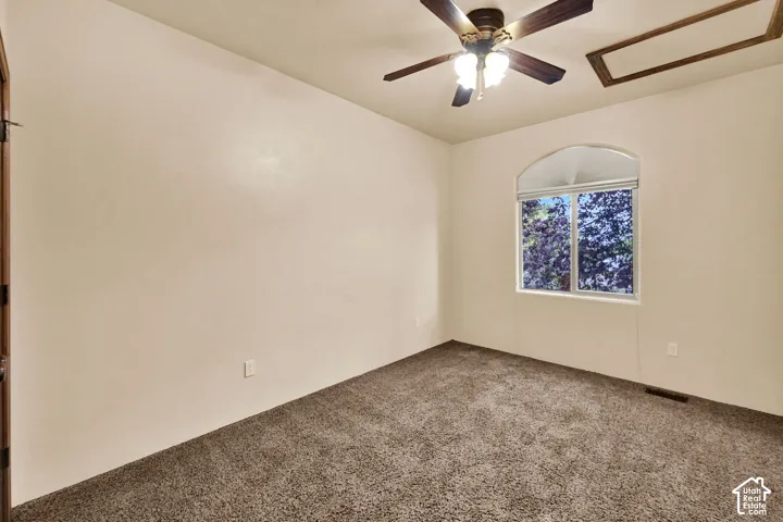 Arch-top window with white trim, brown carpet flooring, and a ceiling fan with light fixture