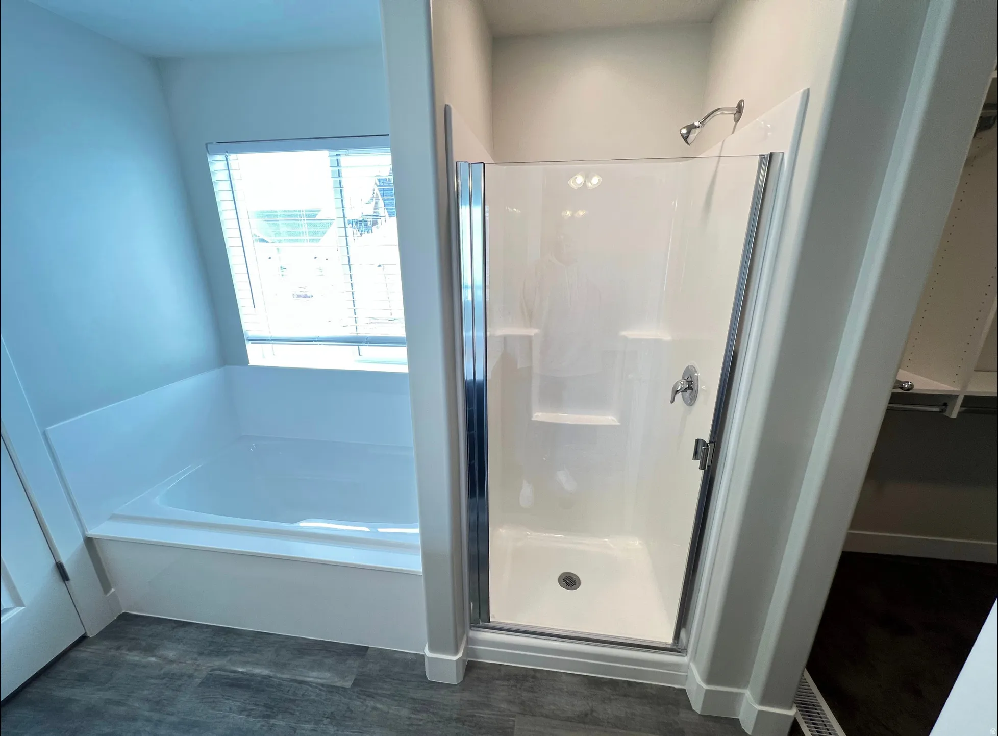 Full bathroom featuring a white tub, separate shower enclosure with chrome hardware, and wood-finish flooring