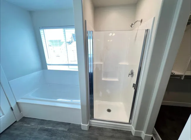 Full bathroom featuring a white tub, separate shower enclosure with chrome hardware, and wood-finish flooring