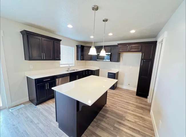 Modern kitchen featuring dark wood cabinetry, white countertops, a central island, stainless steel dishwasher, and recessed lighting