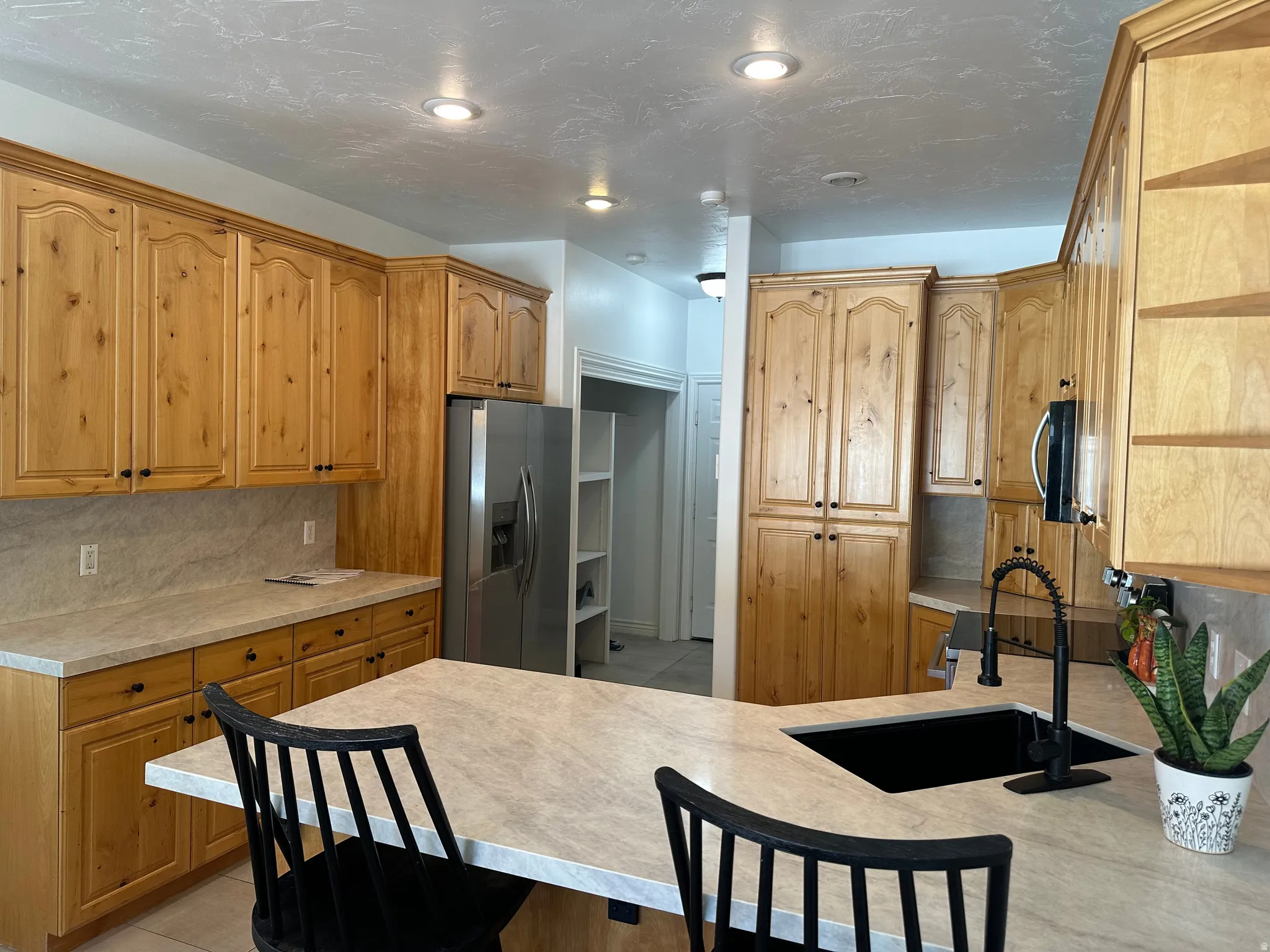 Kitchen featuring wood-finish cabinetry, light-toned countertops, a black sink, and a black pull-down faucet