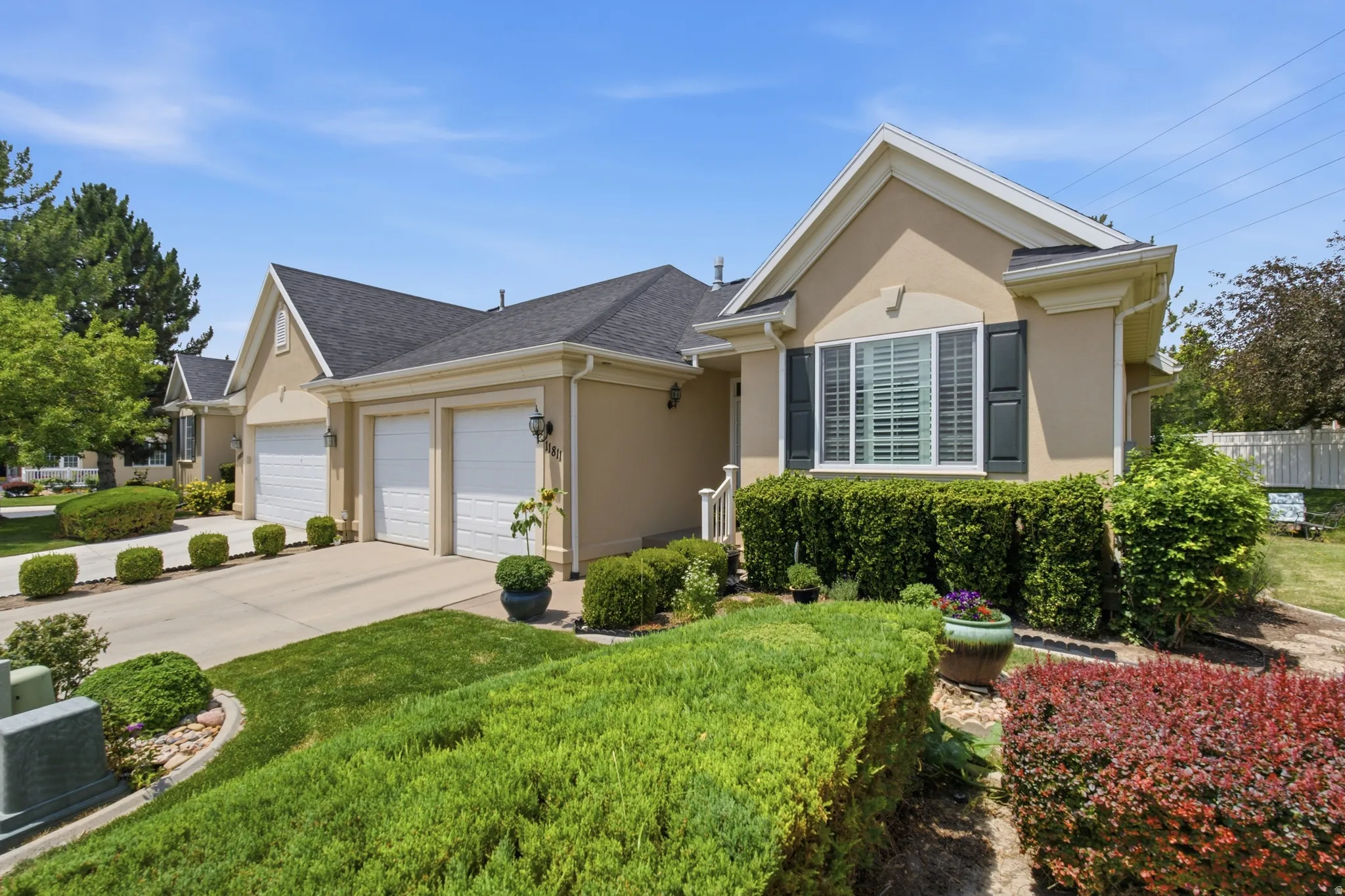 Stucco exterior featuring dual garage doors, a concrete driveway, and mature landscaping