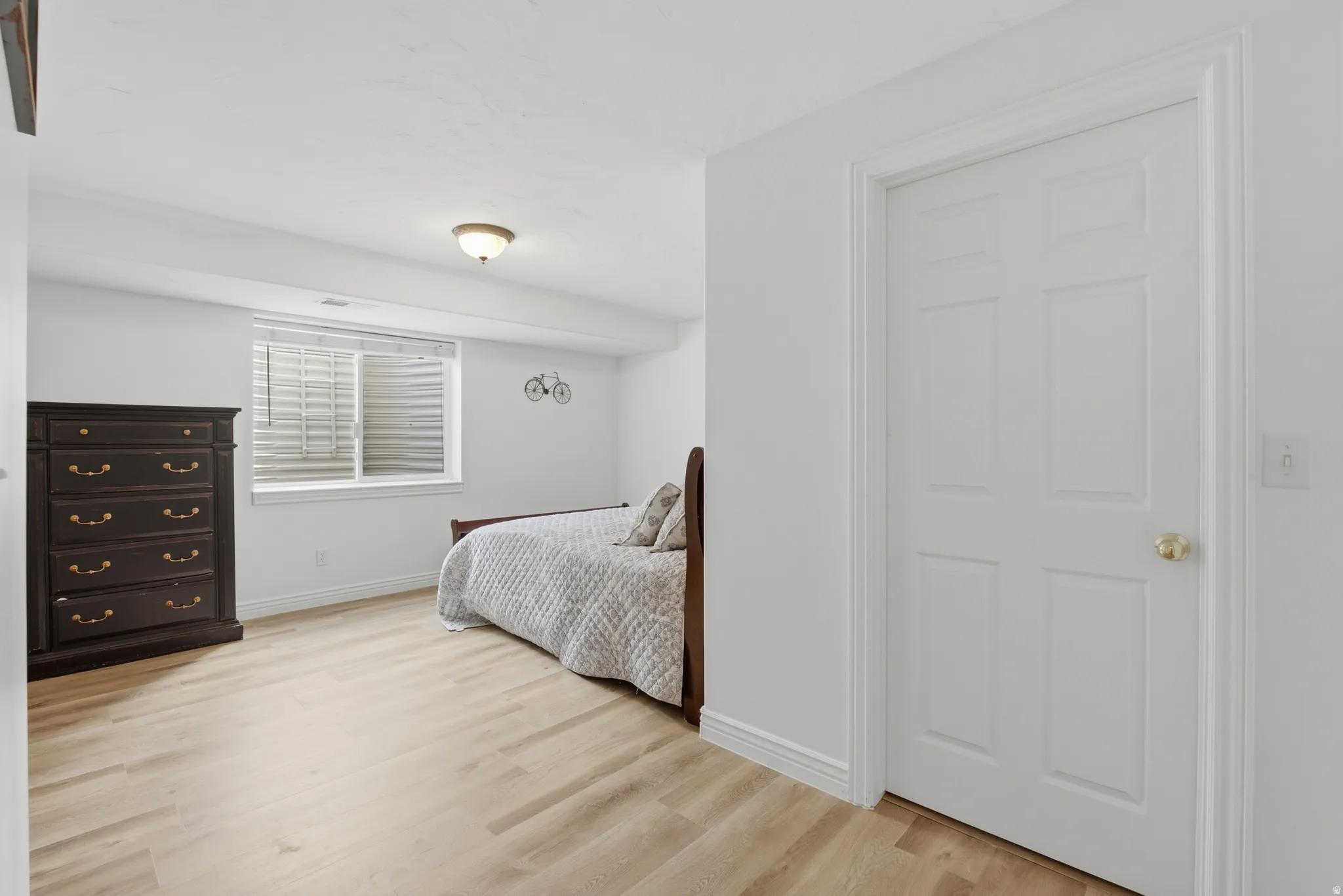 Bright room featuring wood-finish flooring, a white paneled door with brass hardware, and a window with blinds
