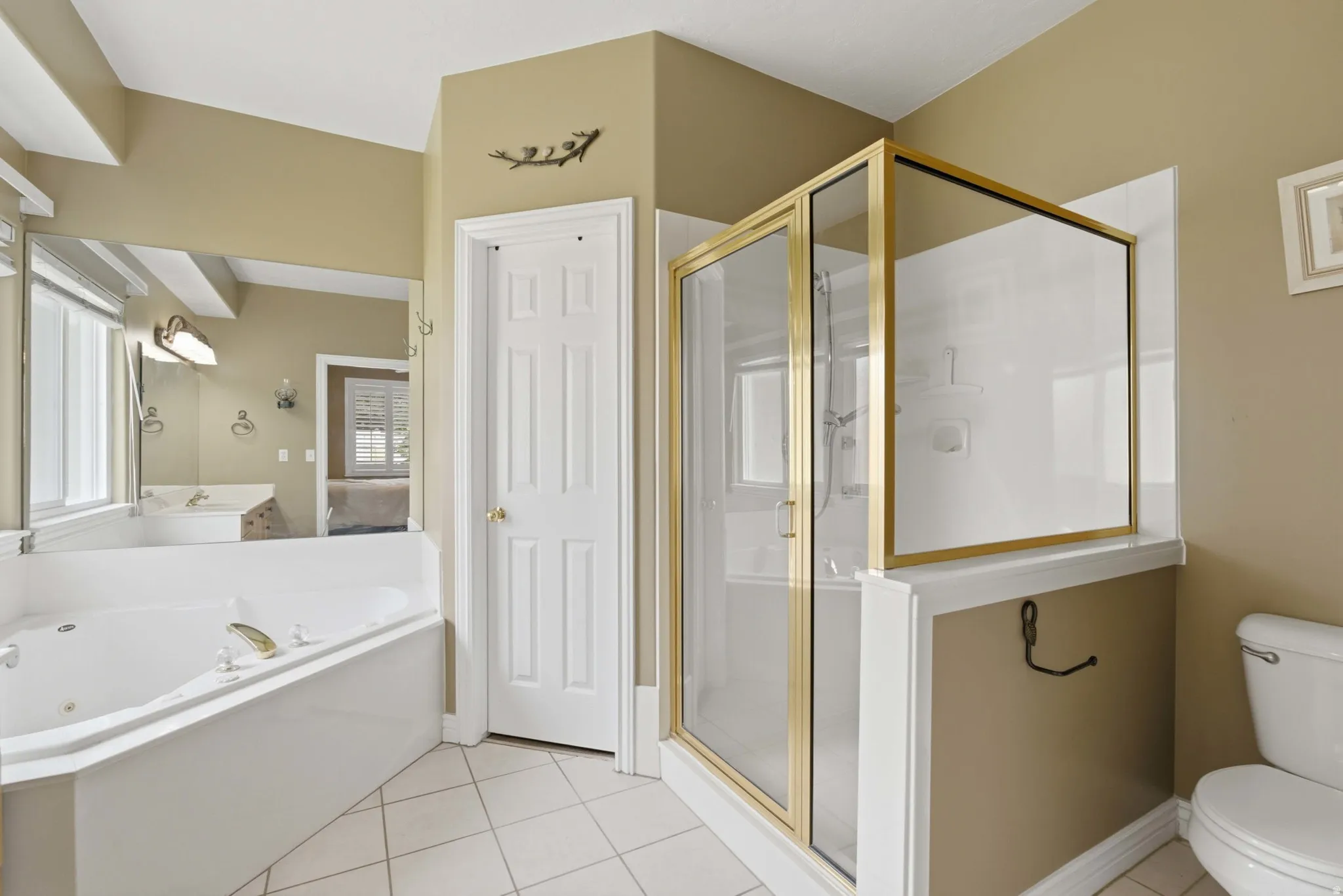 Bathroom featuring a corner jetted tub, a separate shower enclosure with brass-finish framing, white tile flooring, and a six-panel interior door