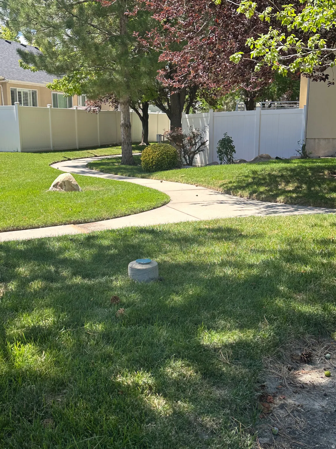 Walking trail pathway, established trees, privacy fencing, manicured lawn, and natural stone accent