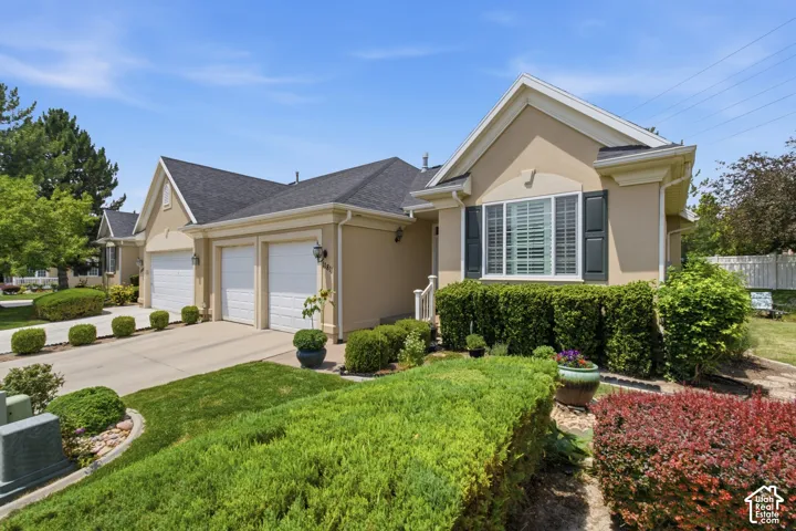 Stucco exterior featuring dual garage doors, a concrete driveway, and mature landscaping