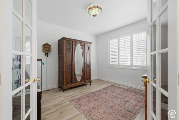 Light-filled room featuring double French doors, wood-finish flooring, a multi-pane window with plantation shutters, and a decorative ceiling light fixture
