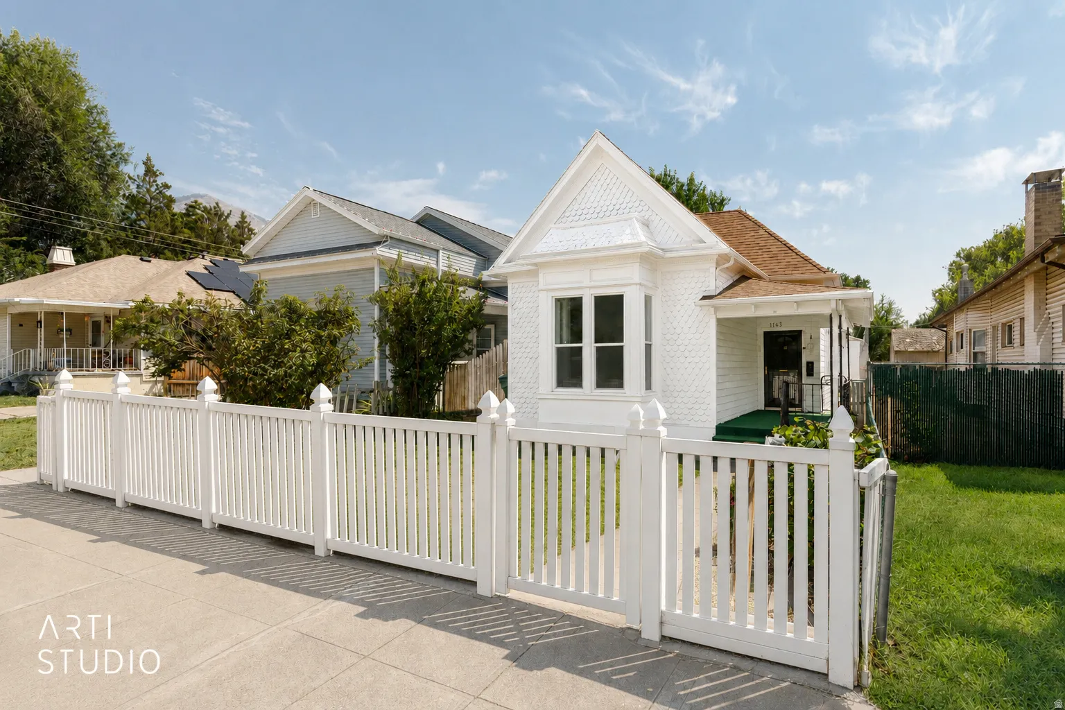 Victorian-style residence featuring a prominent bay window, a covered front porch, and a white picket fence. Virtually cleaned up