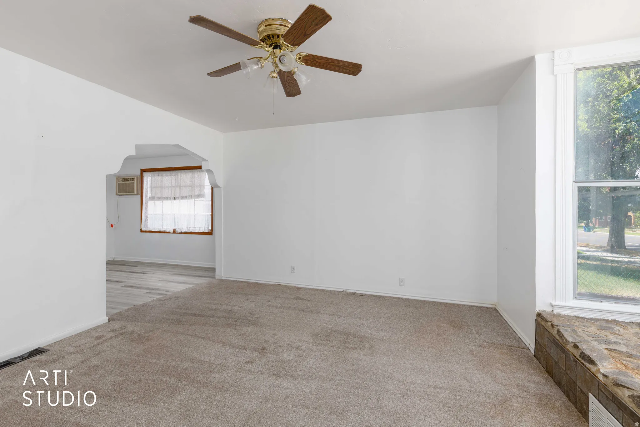 Carpeted living space featuring a ceiling fan with integrated lighting, a large window with white trim, and a tiled window seat