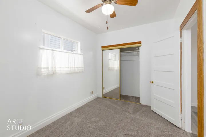 Light grey carpeted flooring, white walls, and a ceiling fan with light fixture