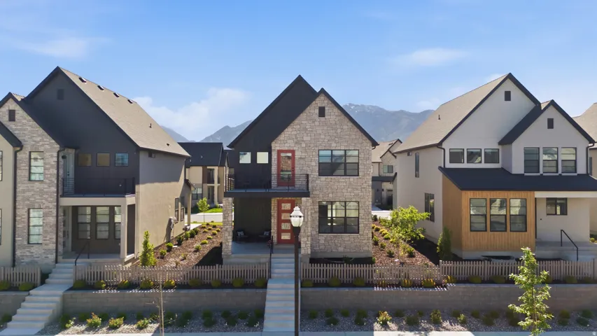 Modern architectural design featuring stone and dark siding, a covered entry, an upper-level balcony, a paved walkway, and tiered landscaping