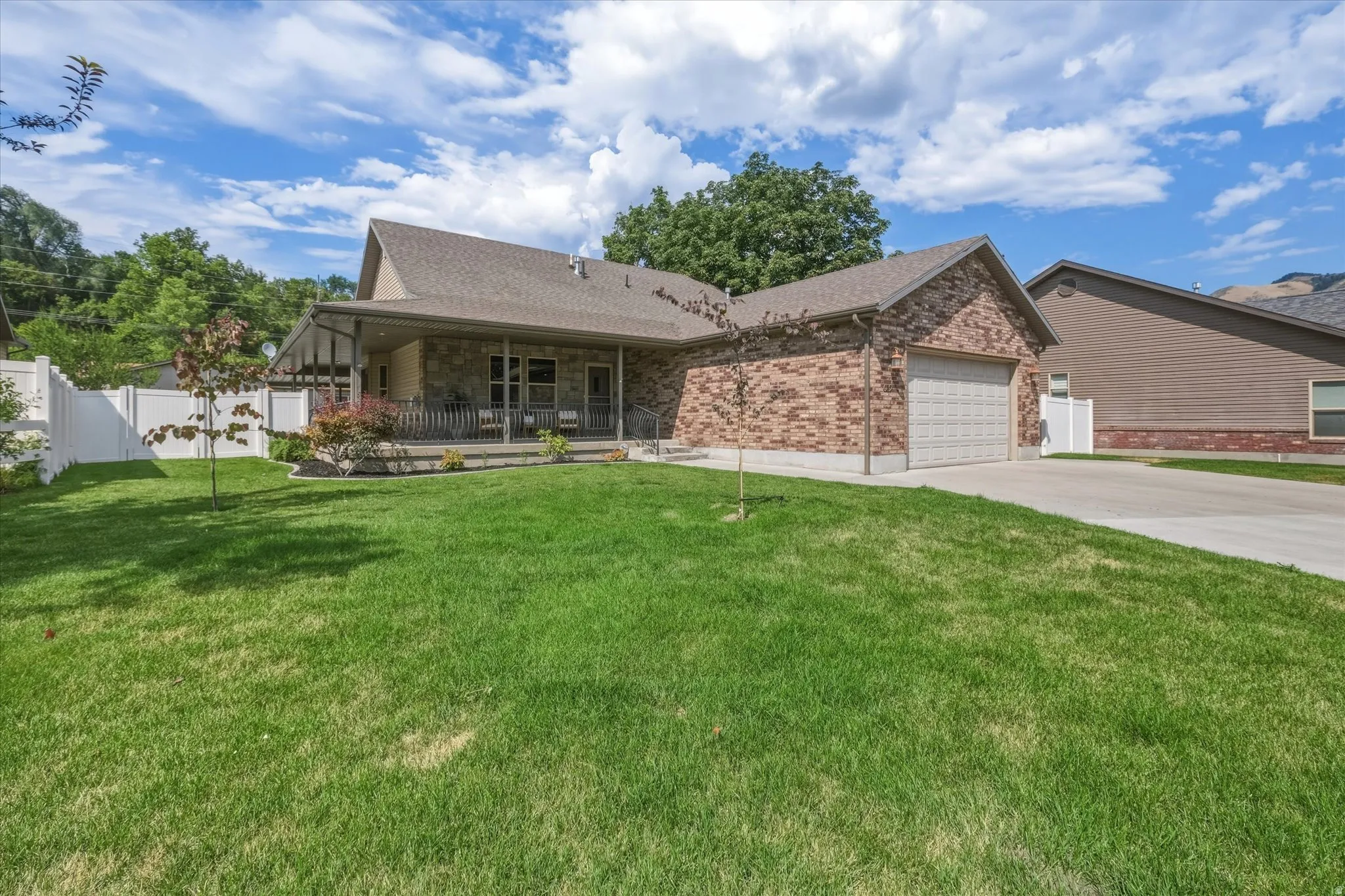 Brick and stone exterior residence featuring an attached garage, covered front porch, and a white privacy fence enclosing the side yard