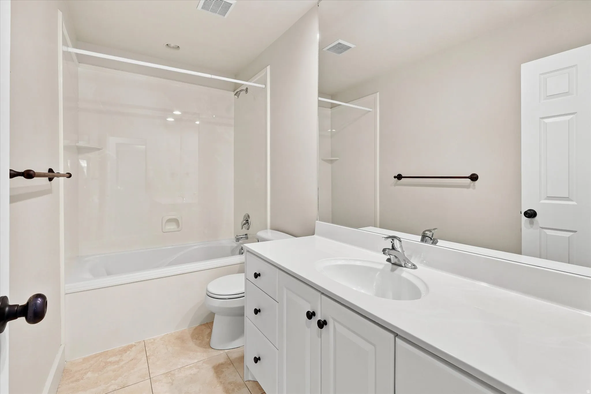 Bathroom featuring a white vanity with integrated sink, a rectangular mirror, a shower-over-tub combination with a clear glass enclosure, and light-toned tile flooring