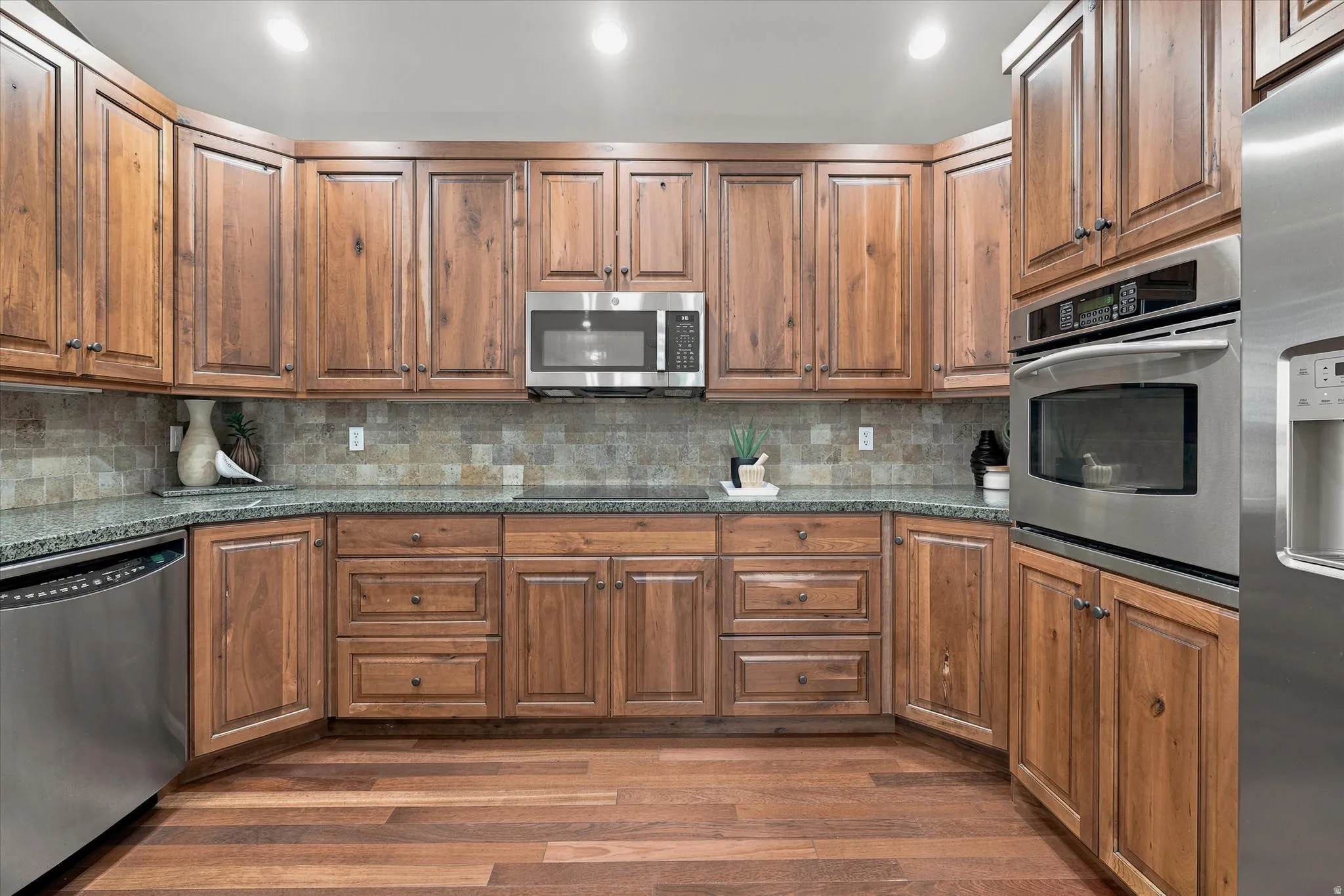 Kitchen featuring wood cabinetry, stainless steel appliances, dark countertops, and a tile backsplash