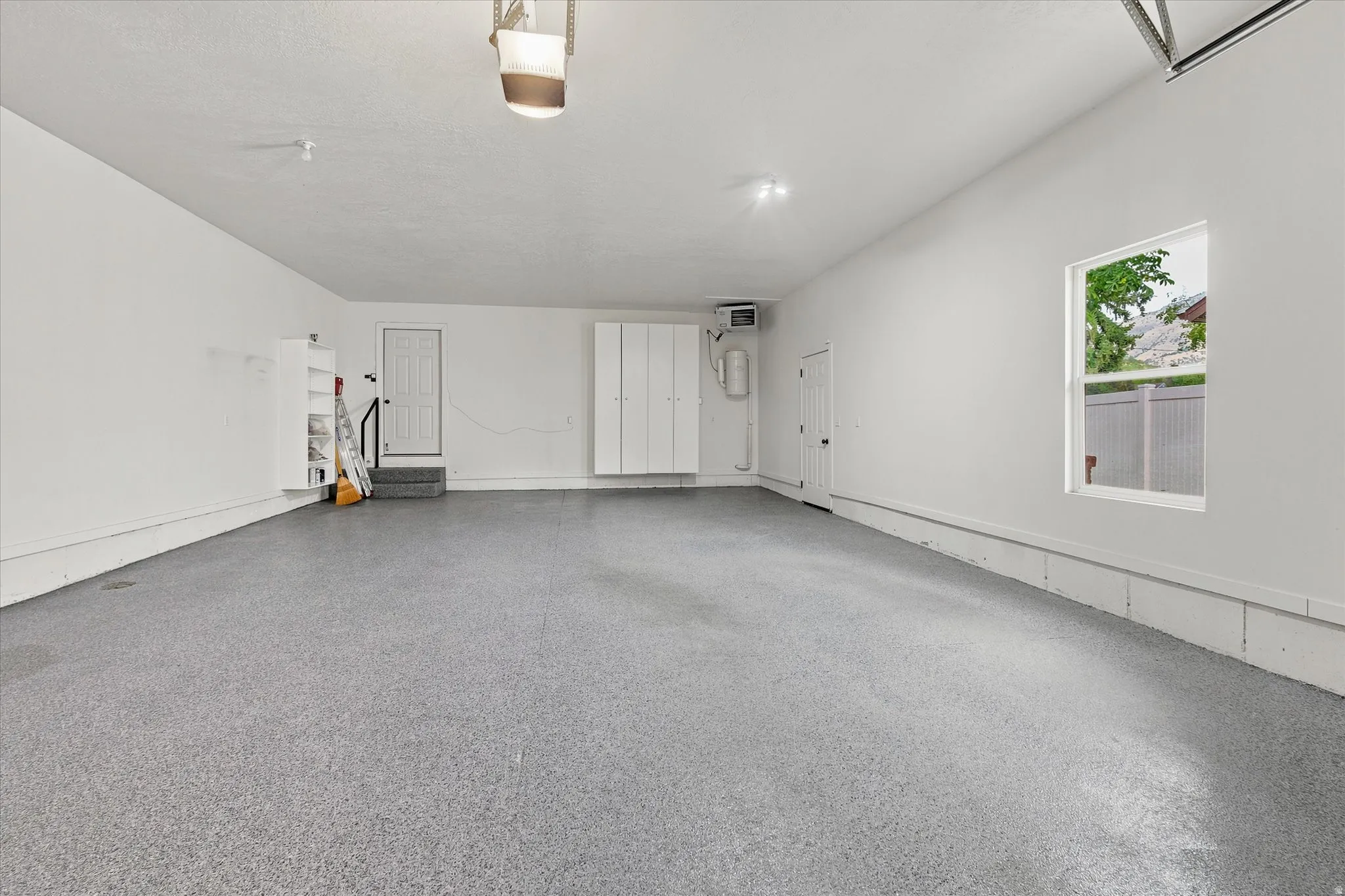 Spacious garage with an epoxy-coated floor, built-in white cabinetry, a window, and a utility sink