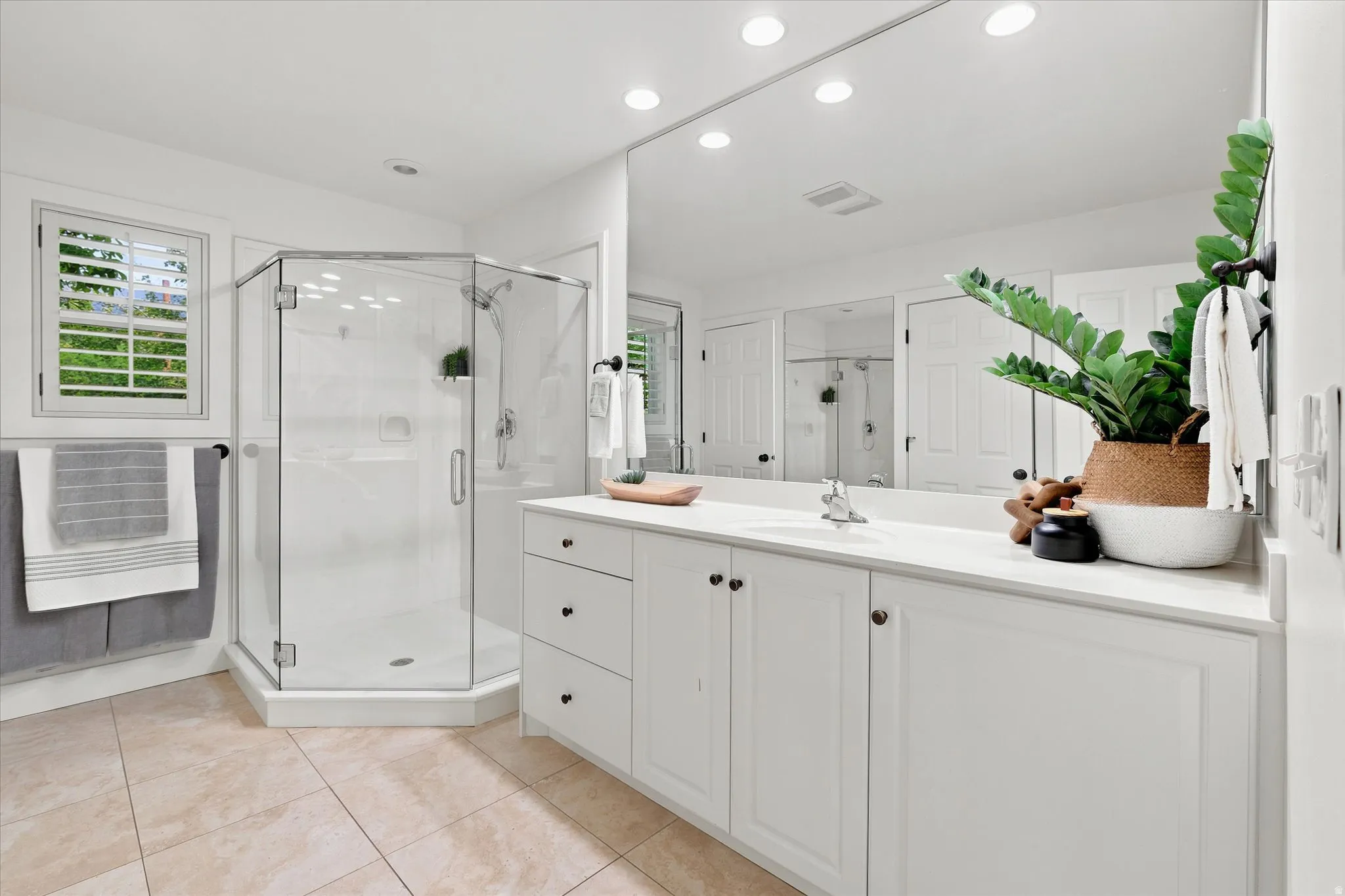 Spacious bathroom featuring a glass-enclosed shower, extensive vanity with white cabinetry, large wall-mounted mirror, and tile flooring
