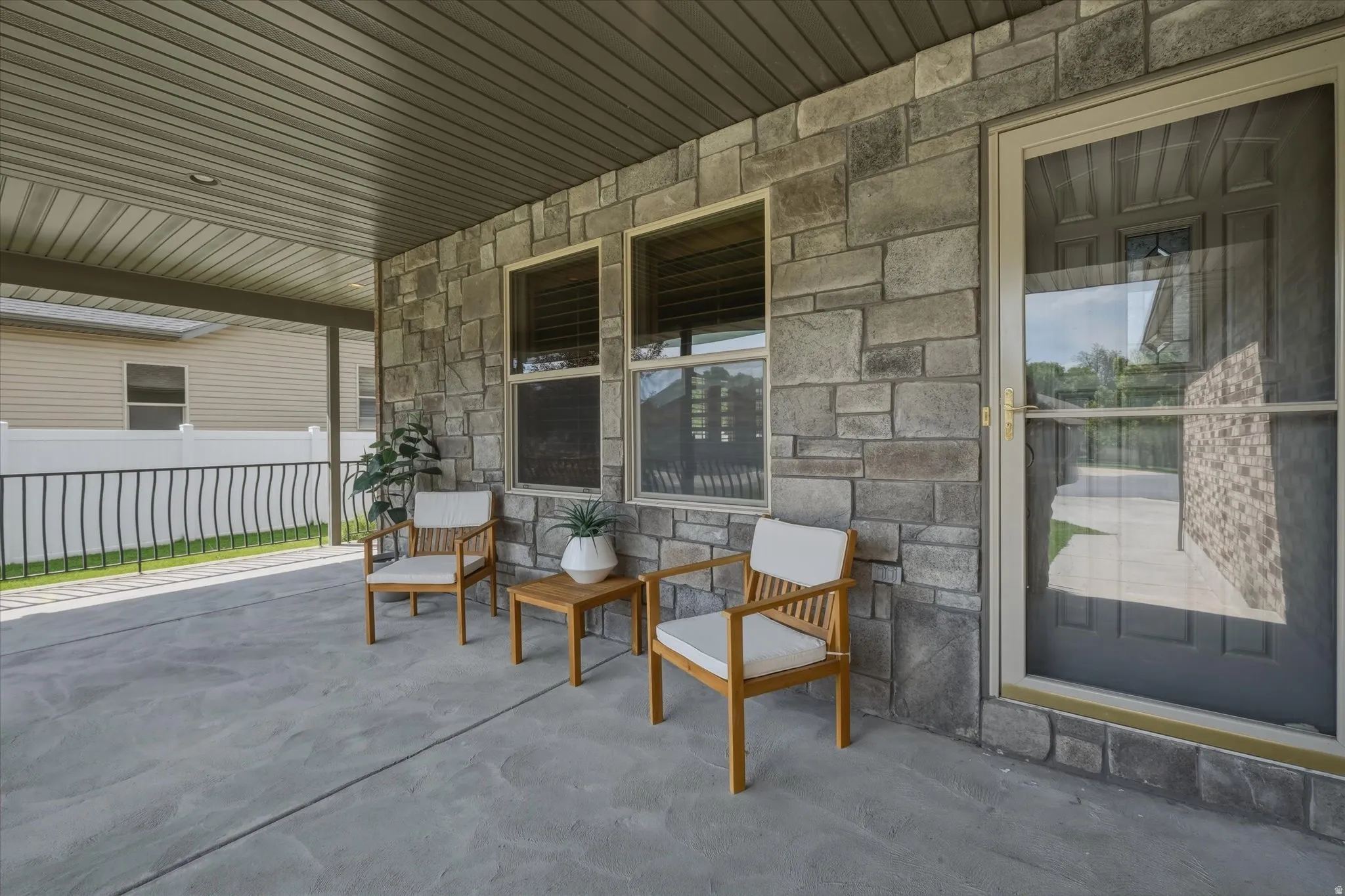 Covered concrete patio featuring a stone veneer exterior wall, multiple windows, and a screen door