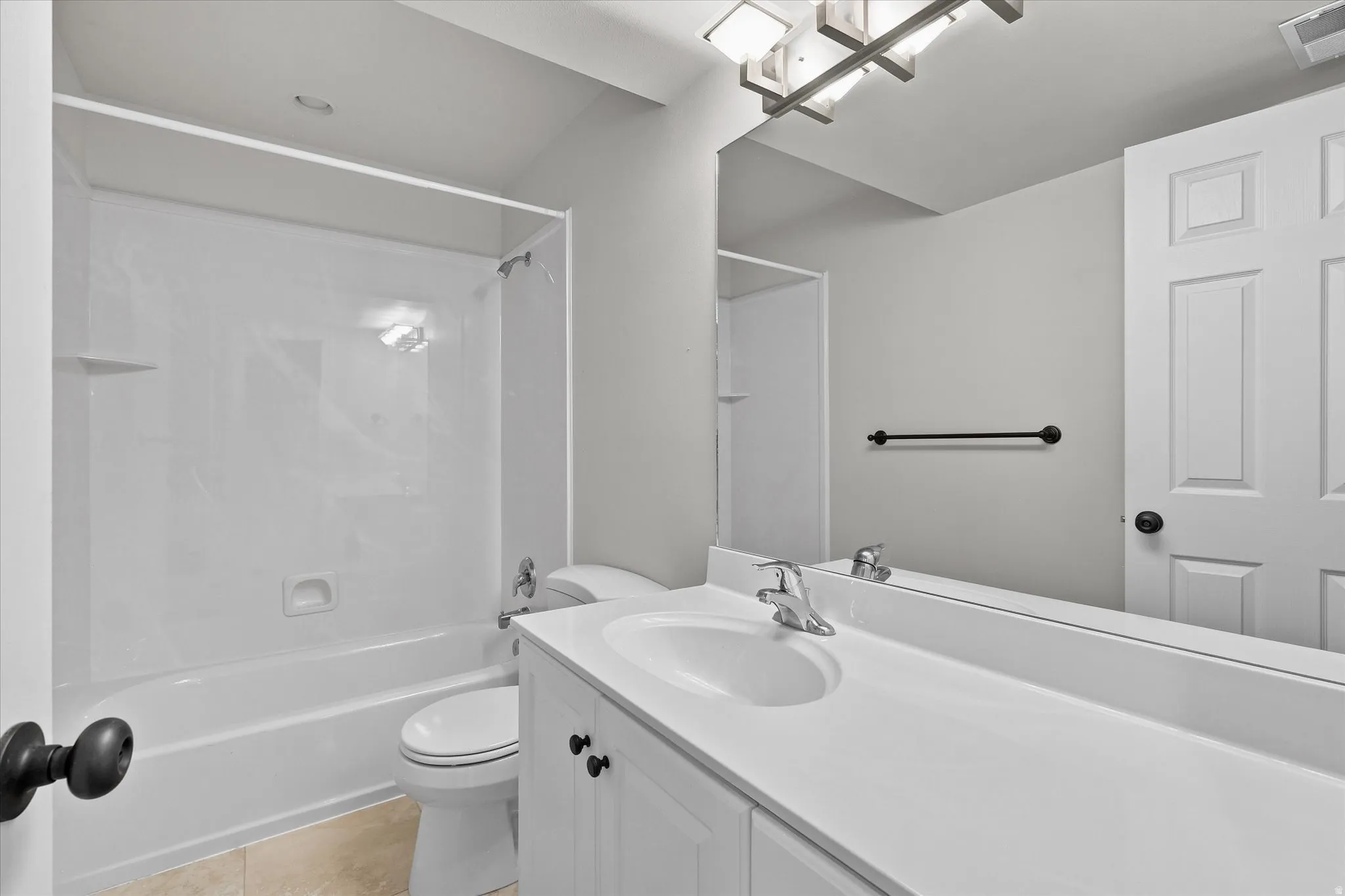 Bathroom featuring a white vanity with integrated sink, chrome faucet, white paneled door, full-width mirror, and a white tub/shower combination with a built-in shelf