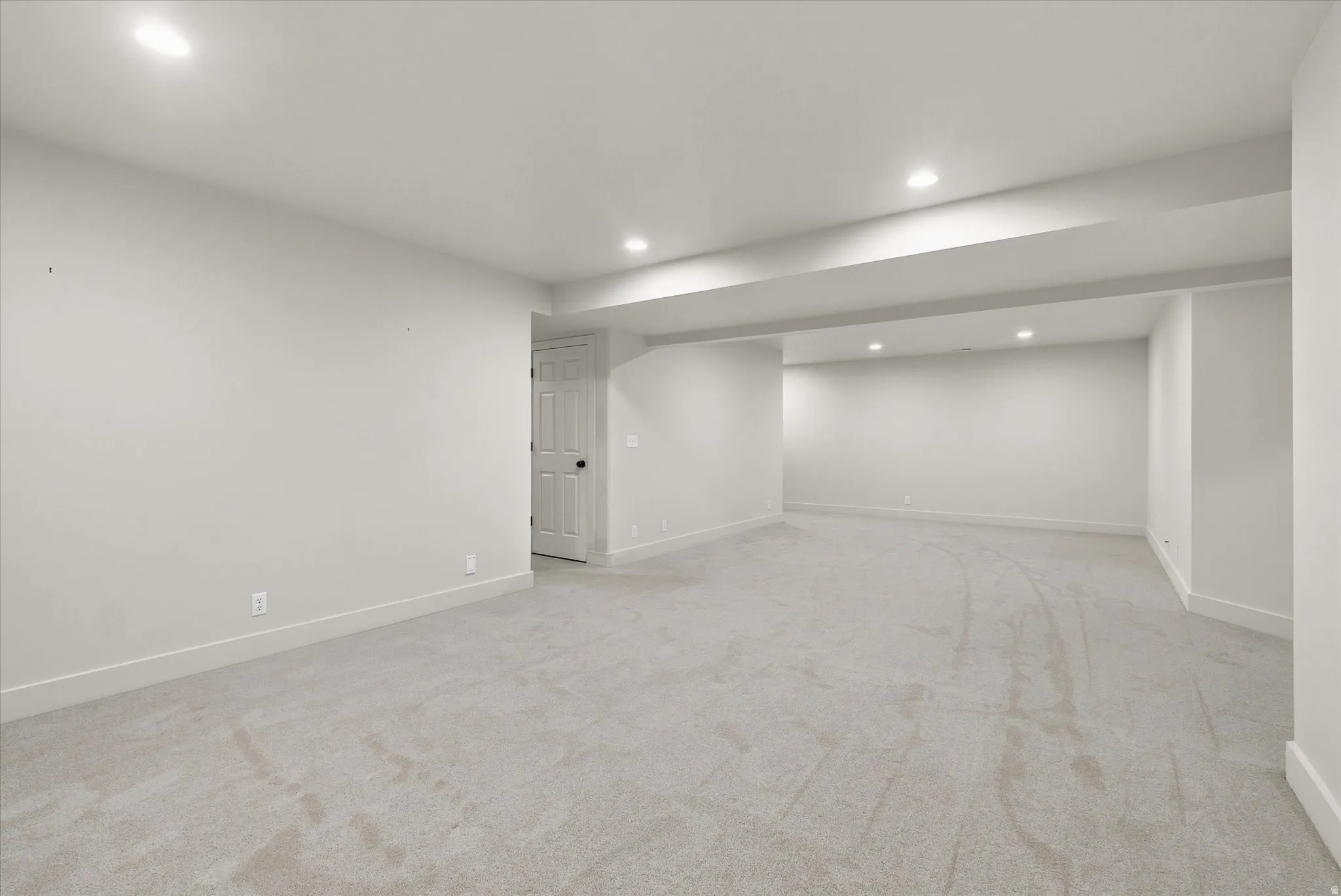 Spacious finished basement featuring light gray carpeting, recessed lighting, white walls, white baseboards, and a white interior door