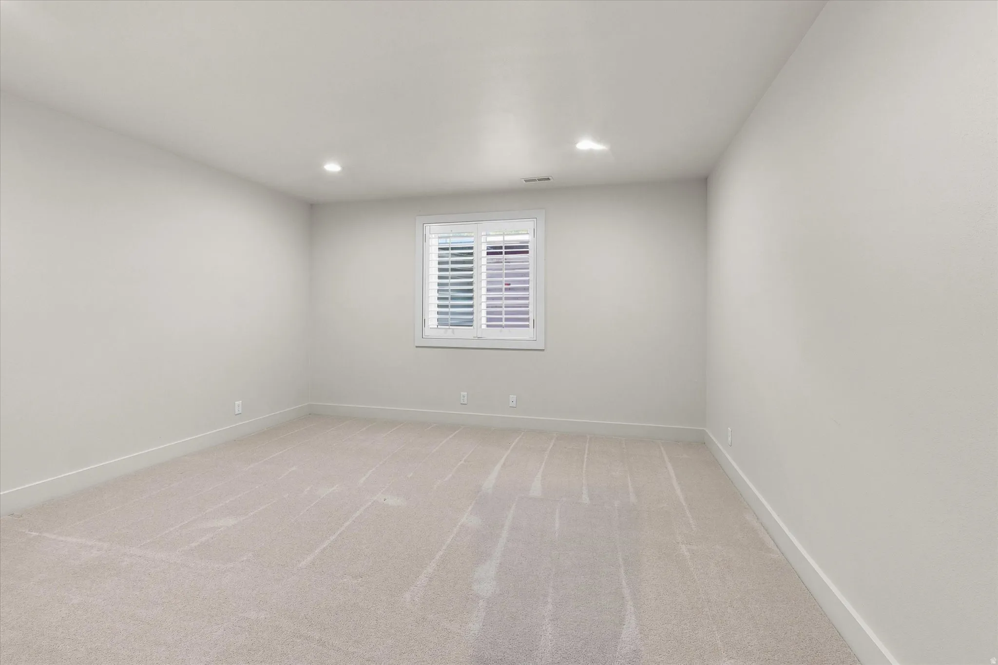 Spacious room with light-toned walls, recessed lighting, and carpet flooring
