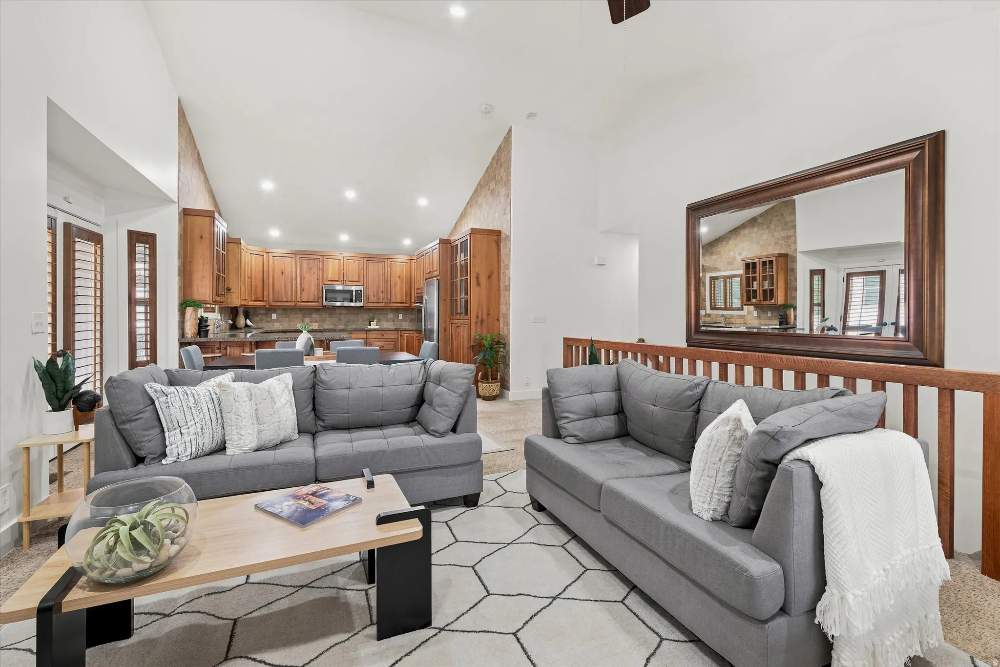 Vaulted ceiling living area featuring recessed lighting, a wooden railing, and a large framed mirror