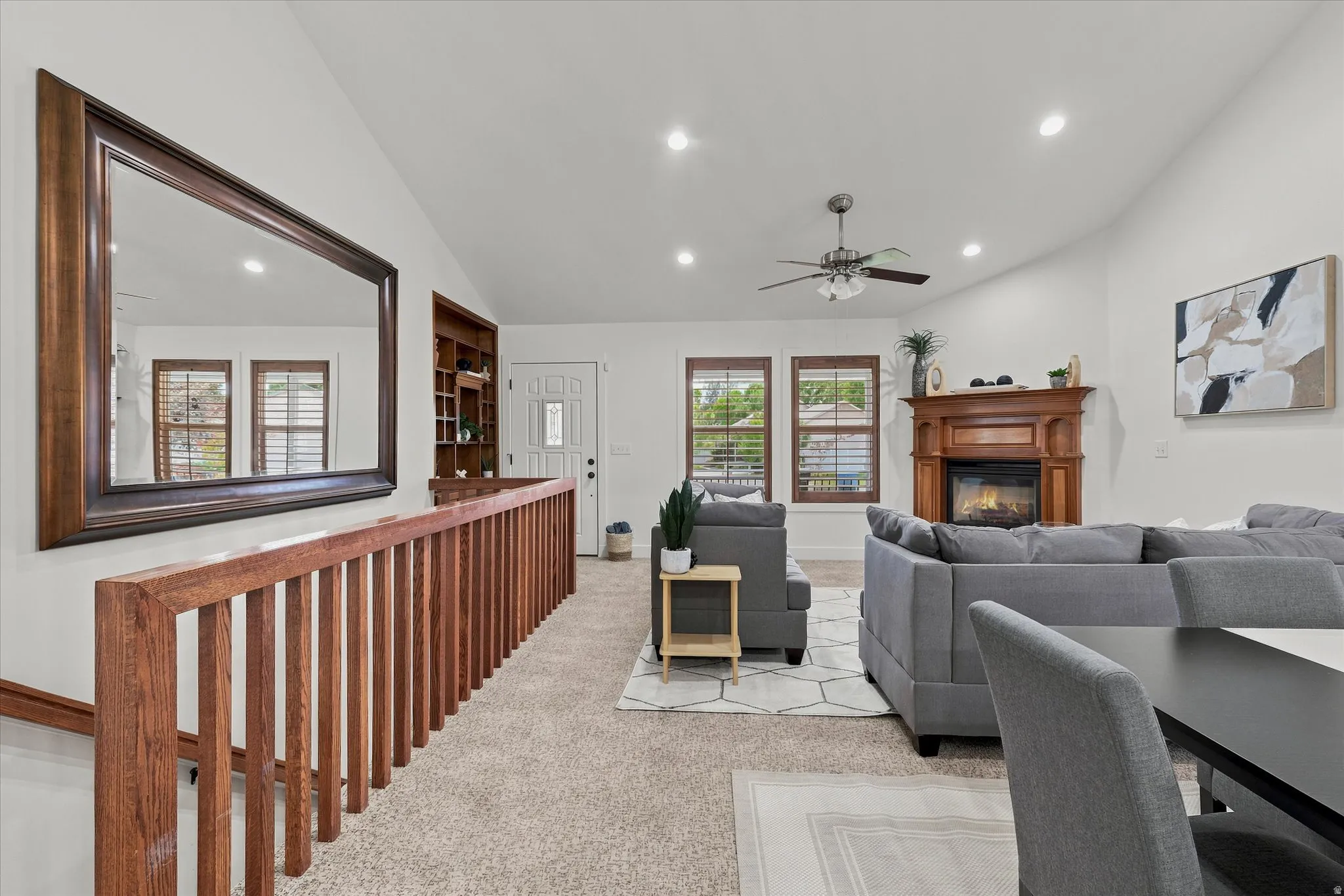 Spacious living area featuring vaulted ceilings, recessed lighting, a fireplace with a decorative wood mantel, and multiple windows with wood blinds
