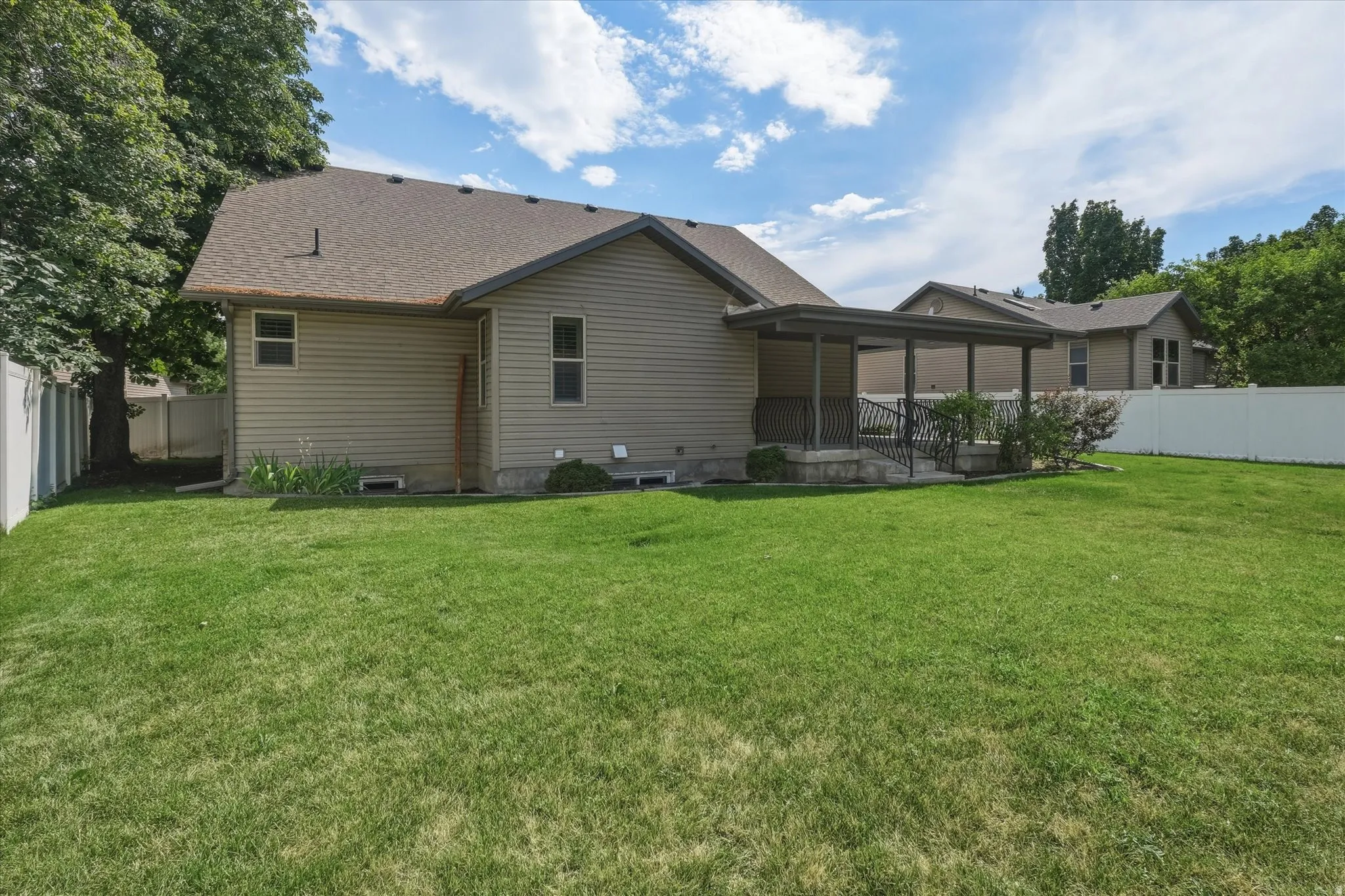 Expansive rear yard featuring green lawn, a covered patio with metal railings, durable vinyl siding, and a white privacy fence