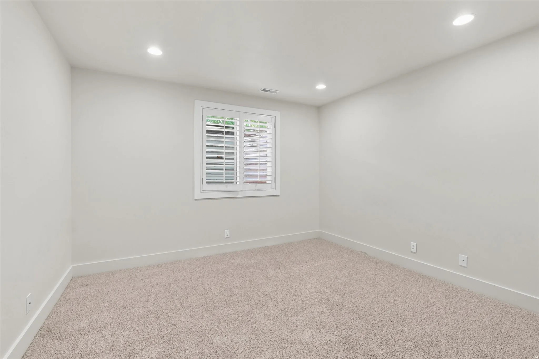Carpeted room with recessed lighting and a window featuring white plantation shutters