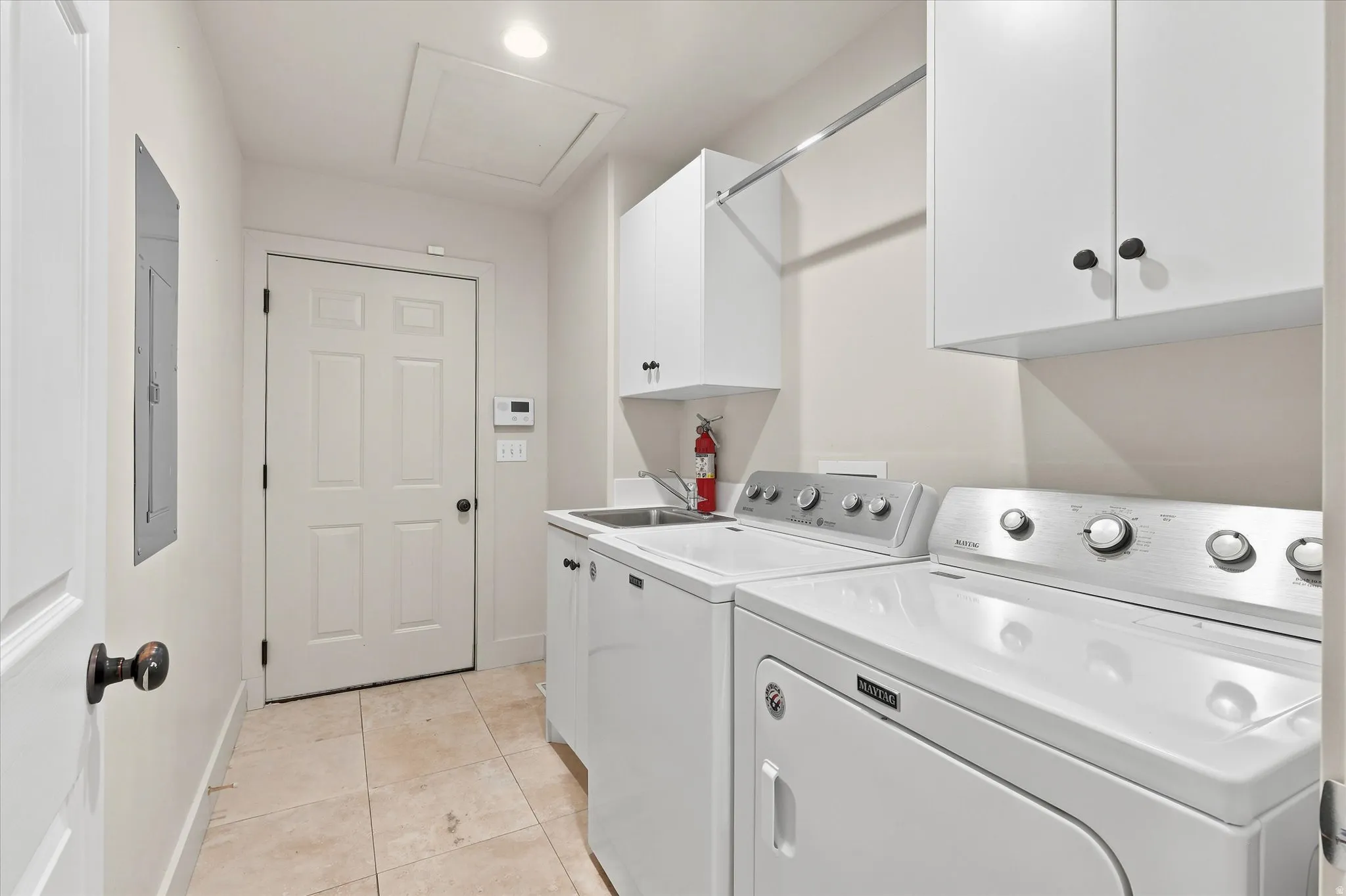 Dedicated laundry room featuring tile flooring, white cabinetry, a utility sink, and a clothes hanging rod