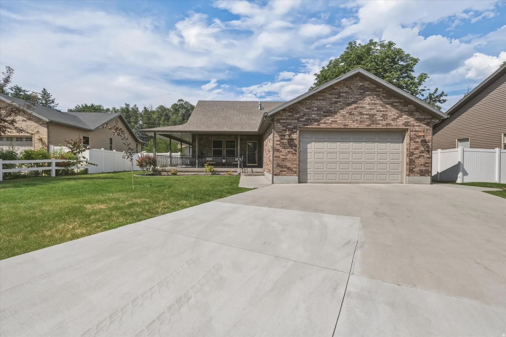 Brick exterior with an attached garage, featuring a concrete driveway, covered porch, and white fencing