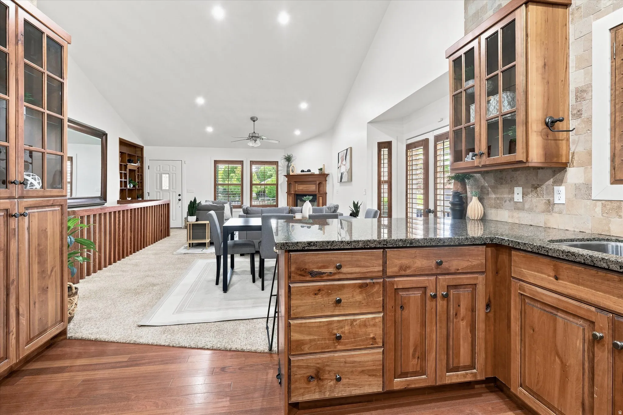 Open-concept interior featuring a kitchen with wood cabinetry and dark countertops, a dining area with a modern table, and a living area with a fireplace