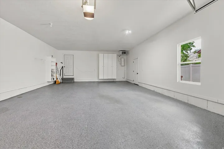 Spacious garage with an epoxy-coated floor, built-in white cabinetry, a window, and a utility sink