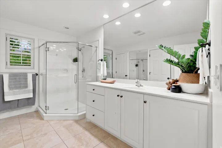 Spacious bathroom featuring a glass-enclosed shower, extensive vanity with white cabinetry, large wall-mounted mirror, and tile flooring