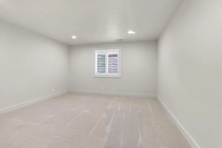 Spacious room with light-toned walls, recessed lighting, and carpet flooring