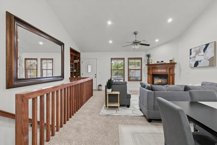 Spacious living area featuring vaulted ceilings, recessed lighting, a fireplace with a decorative wood mantel, and multiple windows with wood blinds