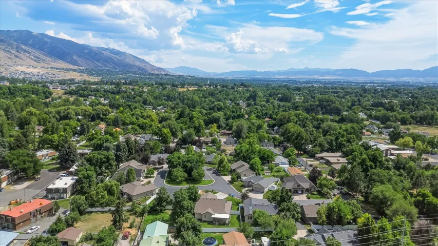 Expansive valley with a verdant tree canopy and residential properties, framed by distant mountains and a blue sky with clouds