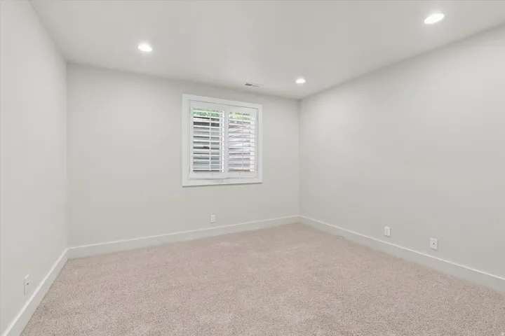 Carpeted room with recessed lighting and a window featuring white plantation shutters