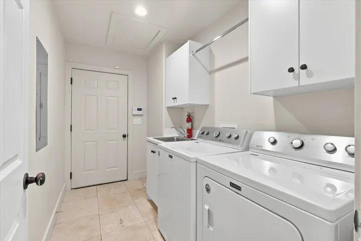 Dedicated laundry room featuring tile flooring, white cabinetry, a utility sink, and a clothes hanging rod