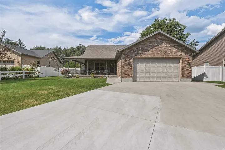 Brick exterior with an attached garage, featuring a concrete driveway, covered porch, and white fencing