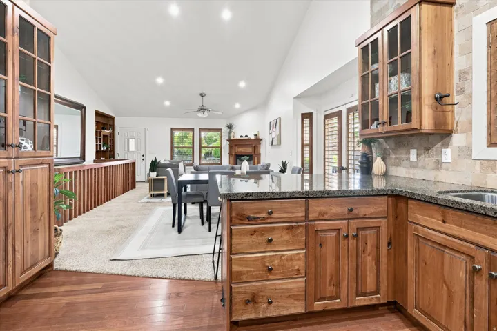 Open-concept interior featuring a kitchen with wood cabinetry and dark countertops, a dining area with a modern table, and a living area with a fireplace
