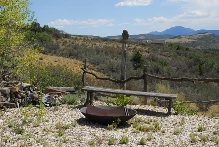 Gravel outdoor area featuring a rustic wood bench, log fencing, and an integrated fire pit