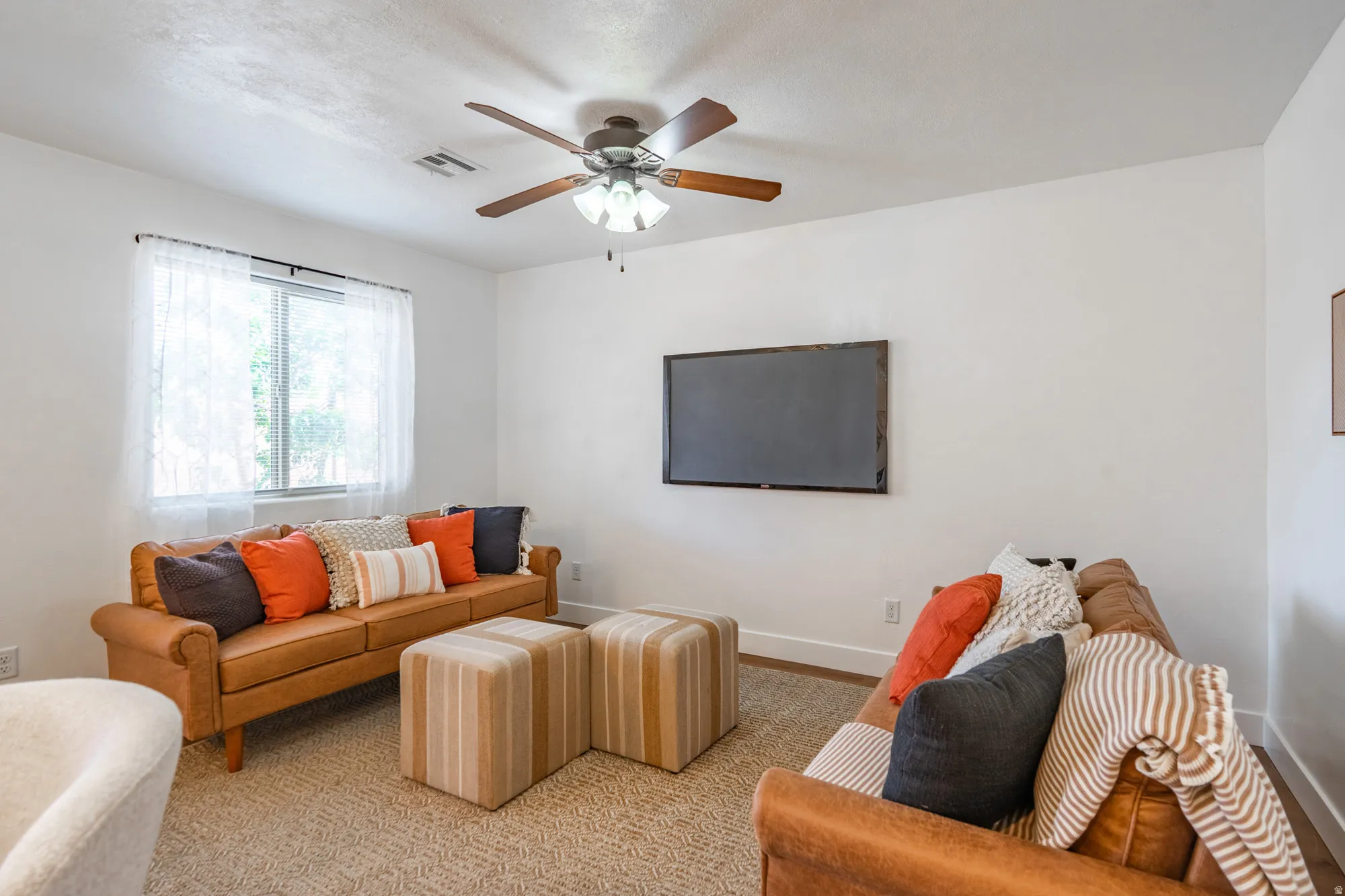 Comfortable living space featuring a ceiling fan with integrated lighting, a large window, white walls, and light-toned patterned carpeting