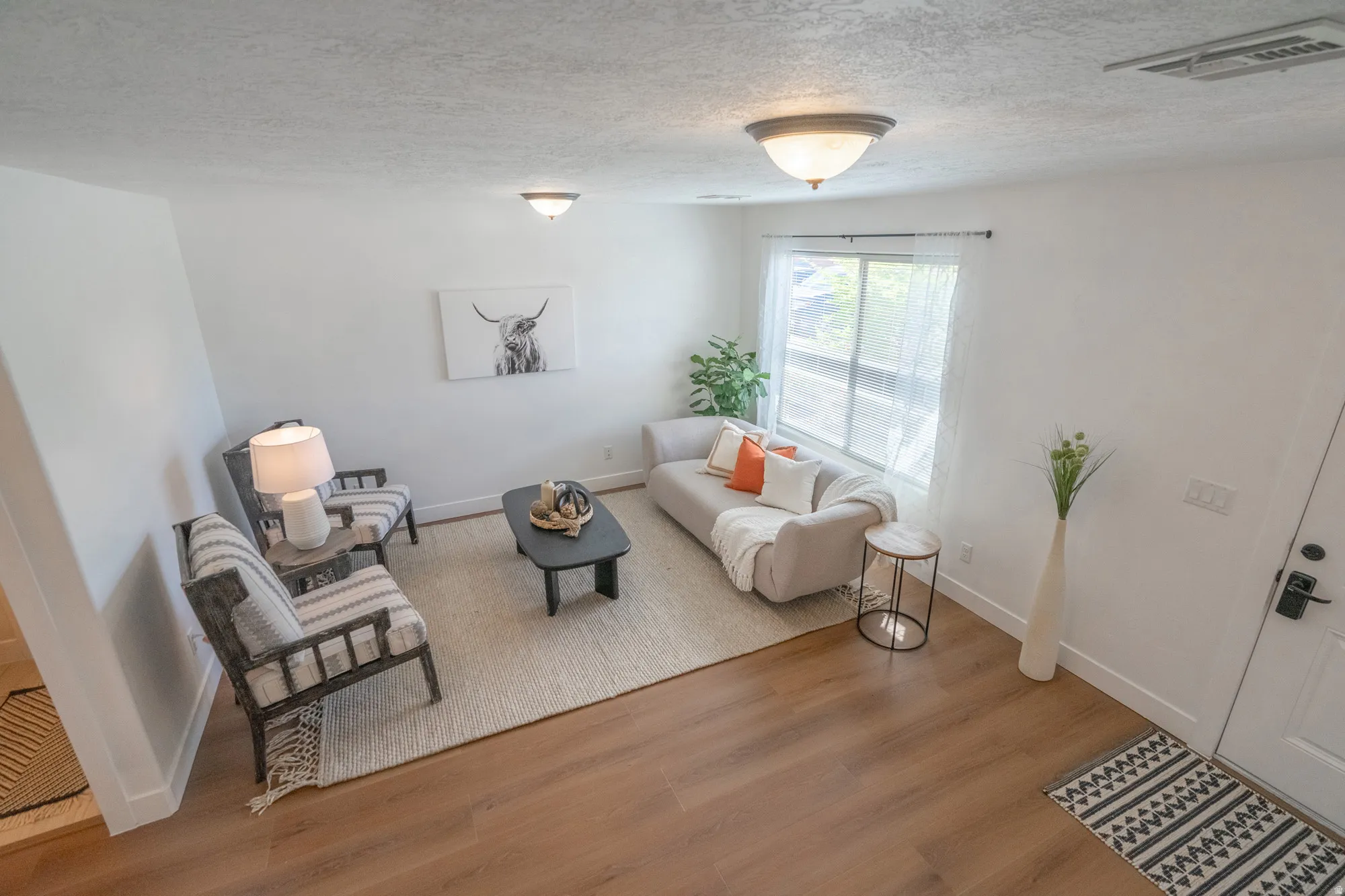 Bright living area featuring wood-finish flooring, white walls, and a large window providing ample natural light